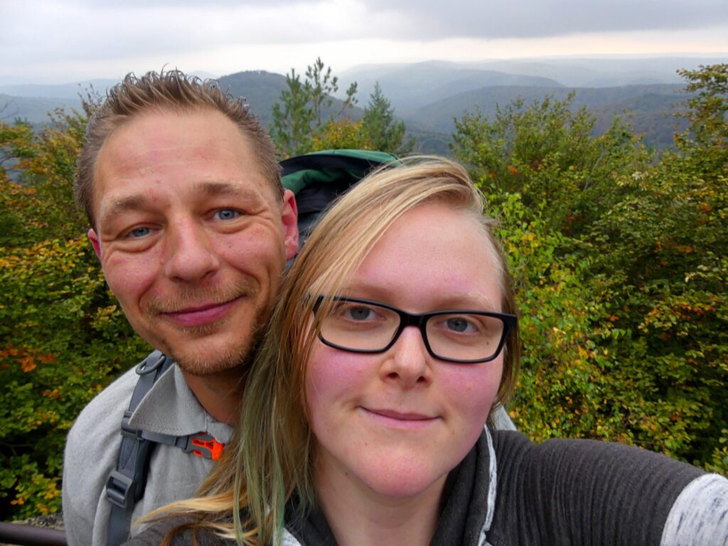 Ein Mann und eine Frau posieren für ein Selfie mit einer Berglandschaft im Hintergrund.
